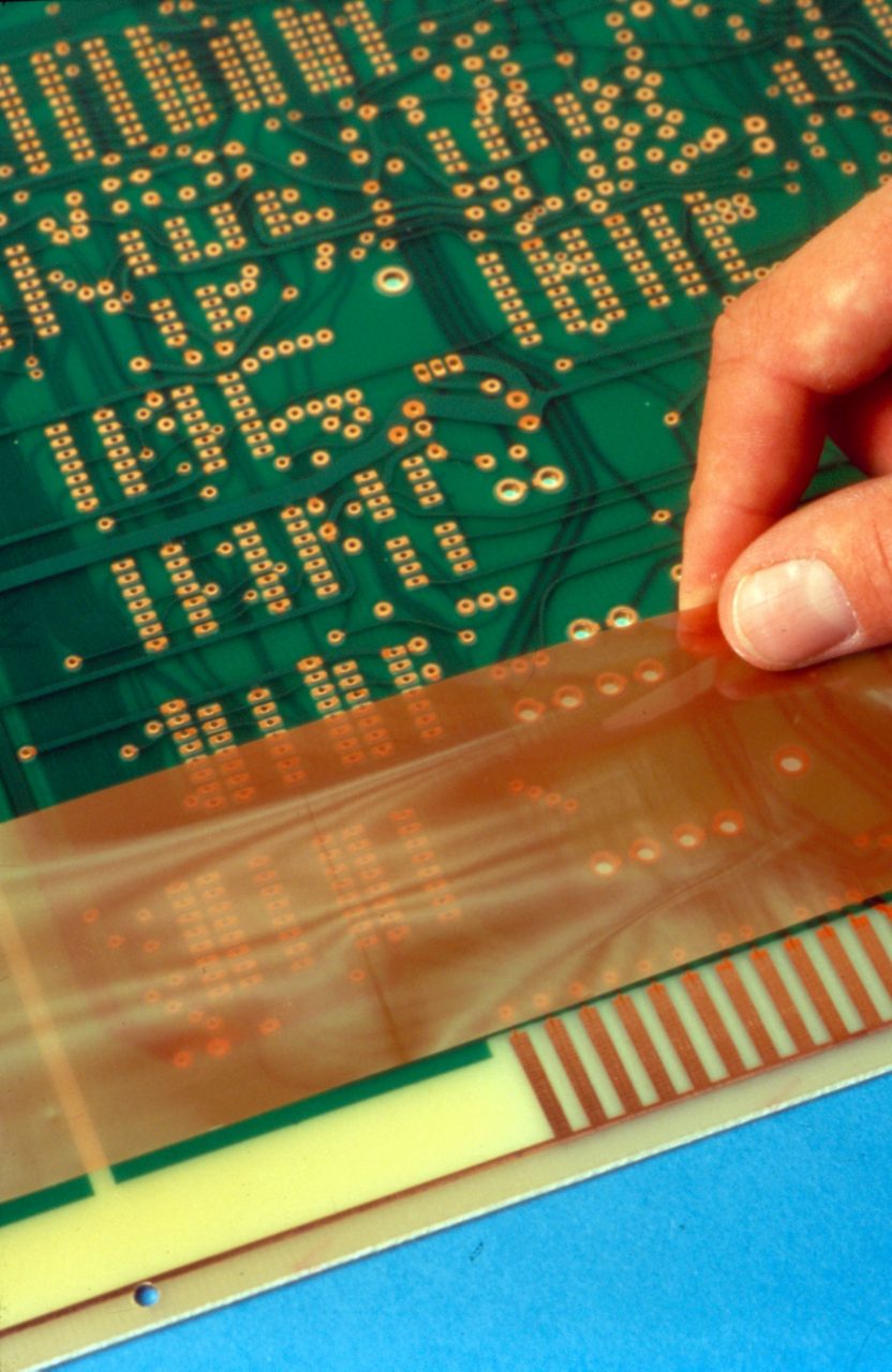 Man's fingers apply pressure-sensitive-adhesive protective film to an electronic circuit board. 