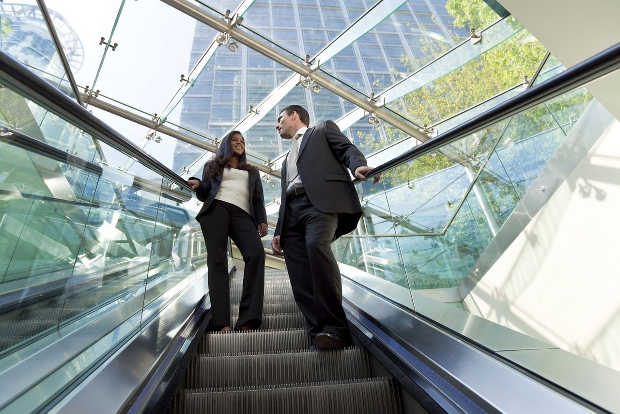 Two employees riding escalator in a high-tech building