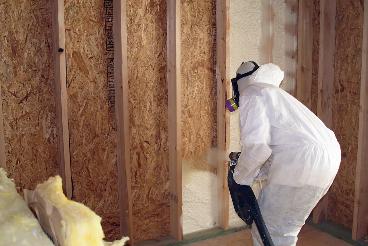 Man in protective white suit and respirator applying insulation with blower 