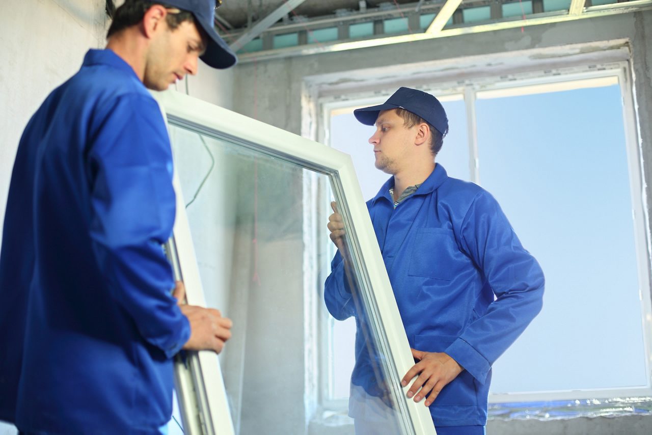 Two men in blue work clothes installing a window 