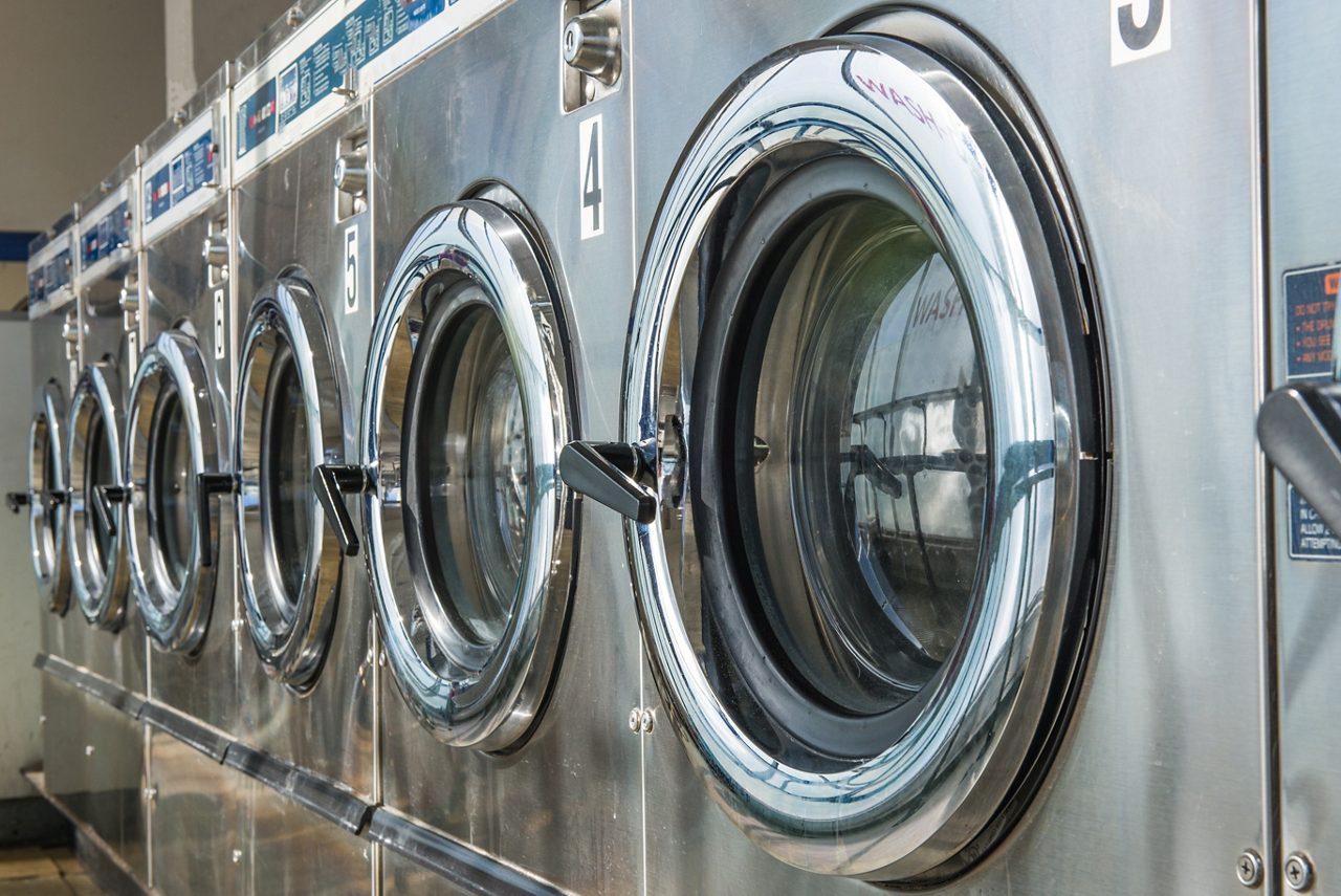 Sequência de 6 máquinas de lavar roupas comerciais com roupas limpas.