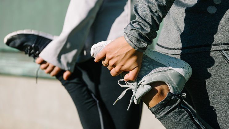 Closeup of two woman grabbing feet to stretch legs before or after a workout or run