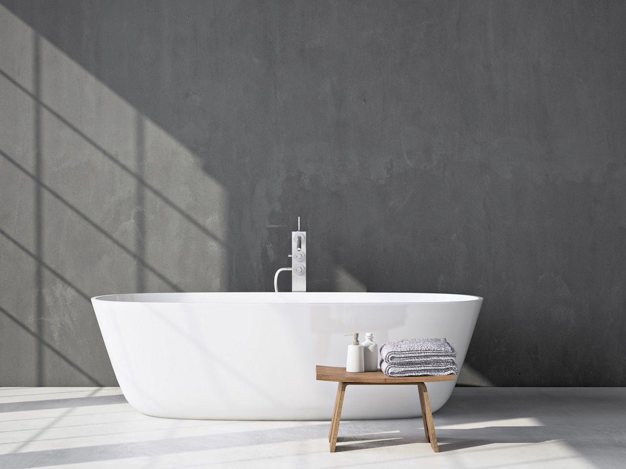 White enamel bathtub against grey wall with wooden stool holding towels and toiletry bottles