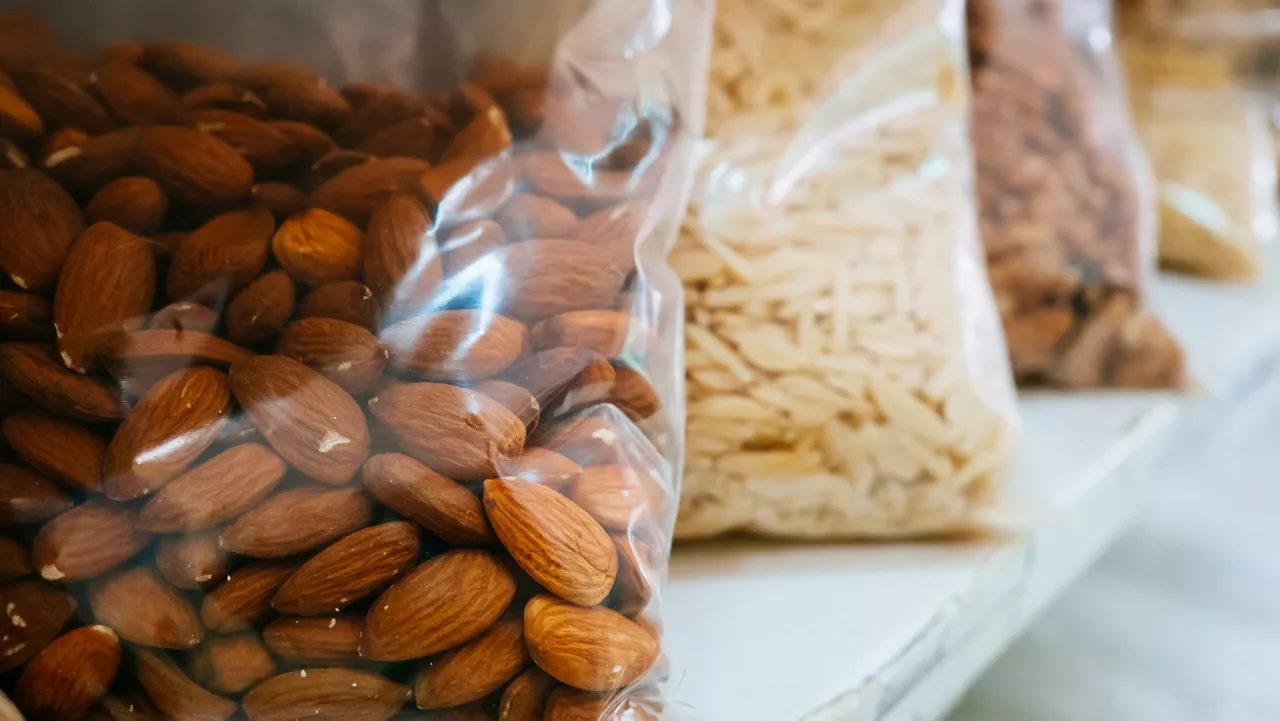 Plastic bag of almonds on a shelf with other bags of nuts.