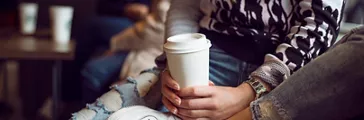 Two people sitting holding a paper coffee cup