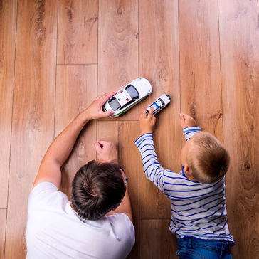 padre con su hijo jugando con autos en el piso de madera