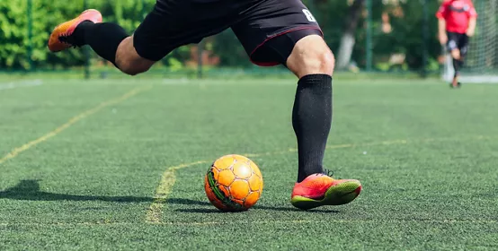 Male soccer player kicking yellow soccer ball on artificial turf