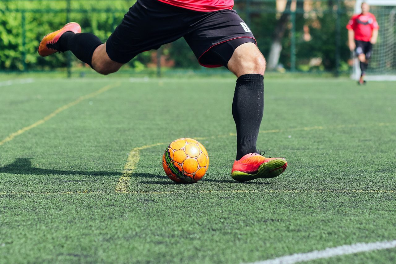 Jogador de futebol chuta uma bola em grama artificial