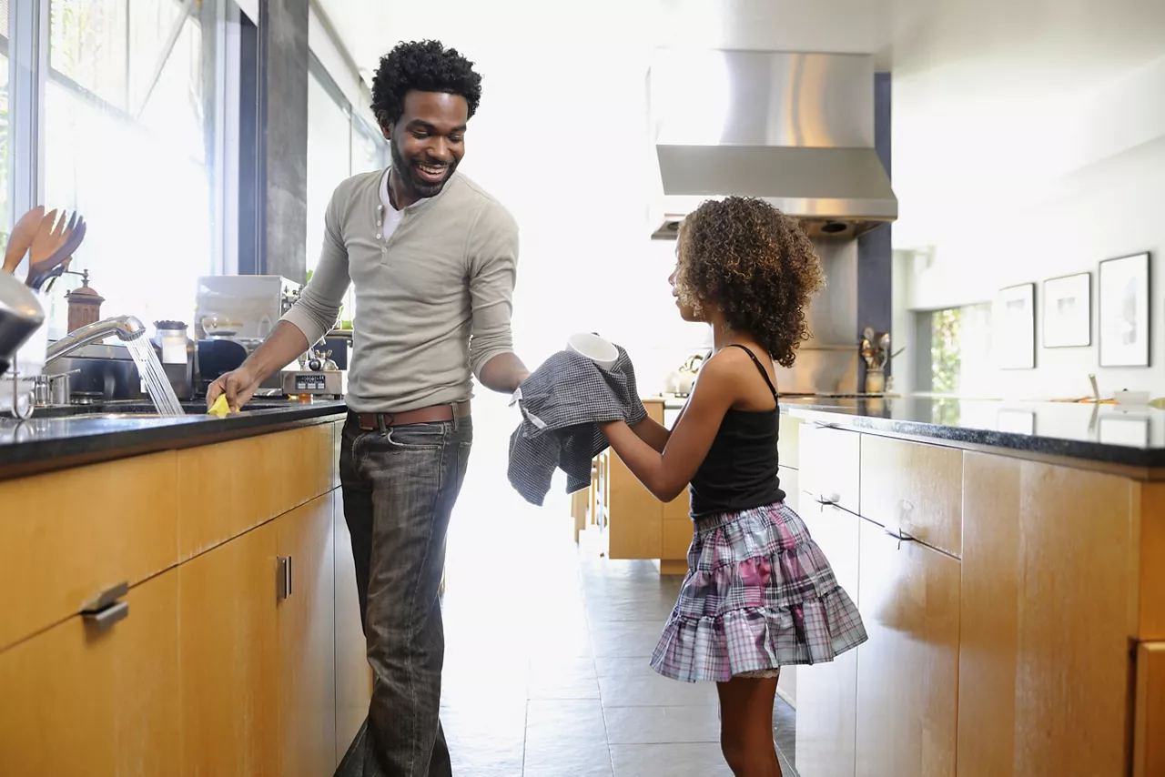 Father and daughter washing dishes in a large modern kitchen.