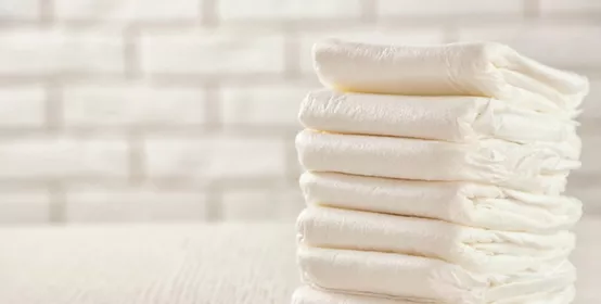 Stack of white diapers on white wood table with white brick wall in background