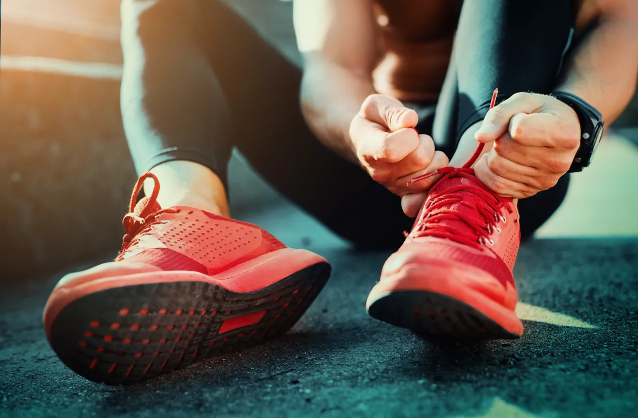 Man tying red jogging shoes, sitting on the ground.