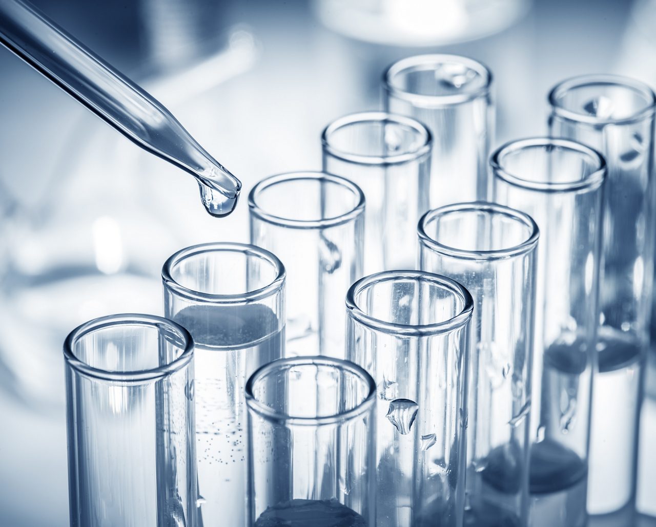 Test tubes lined up in two rows with pipette dripping clear liquid