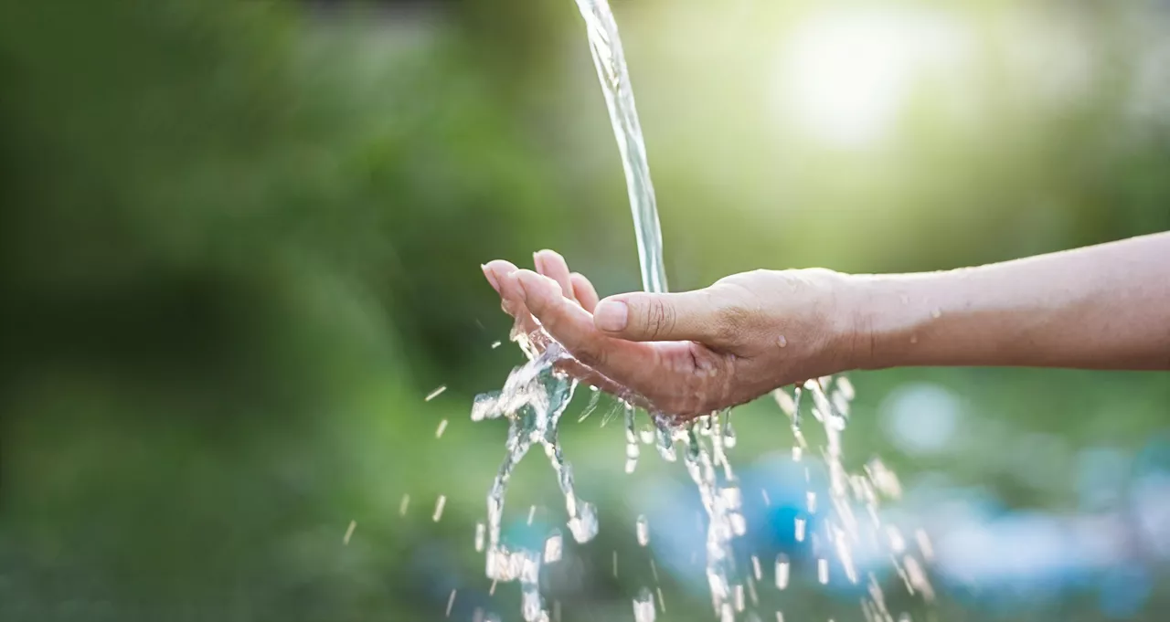 Water pouring in woman's hand on nature background 