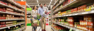 Happy family with child and shopping cart buying food at grocery store or supermarket.