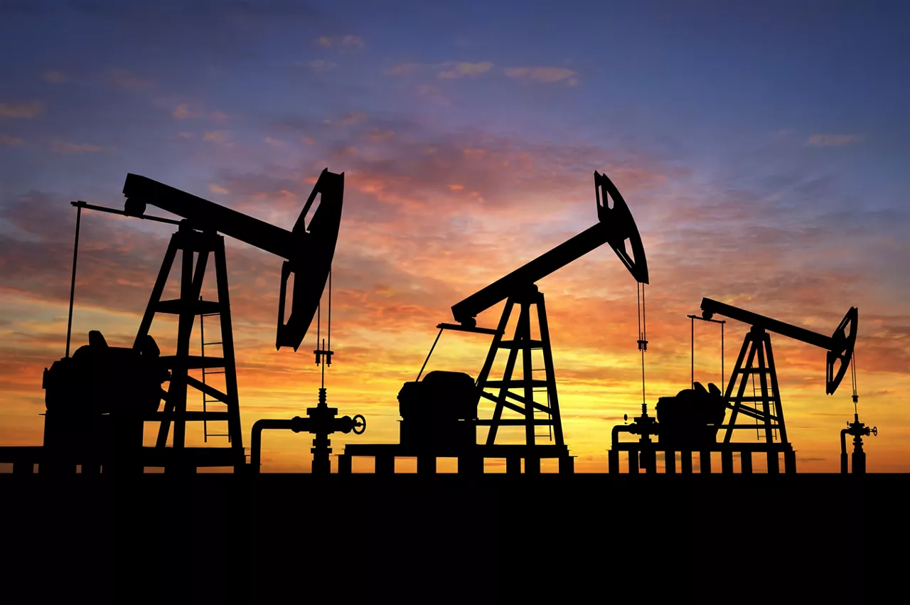 Silhouette of three oil pumps over orange sky