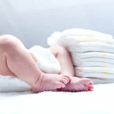 Bebê usando fralda deitada de costas ao lado de uma pilha de fraldas