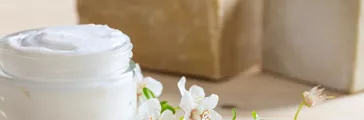 Glass jar of moisturizing cream and almond blossoms on wooden background