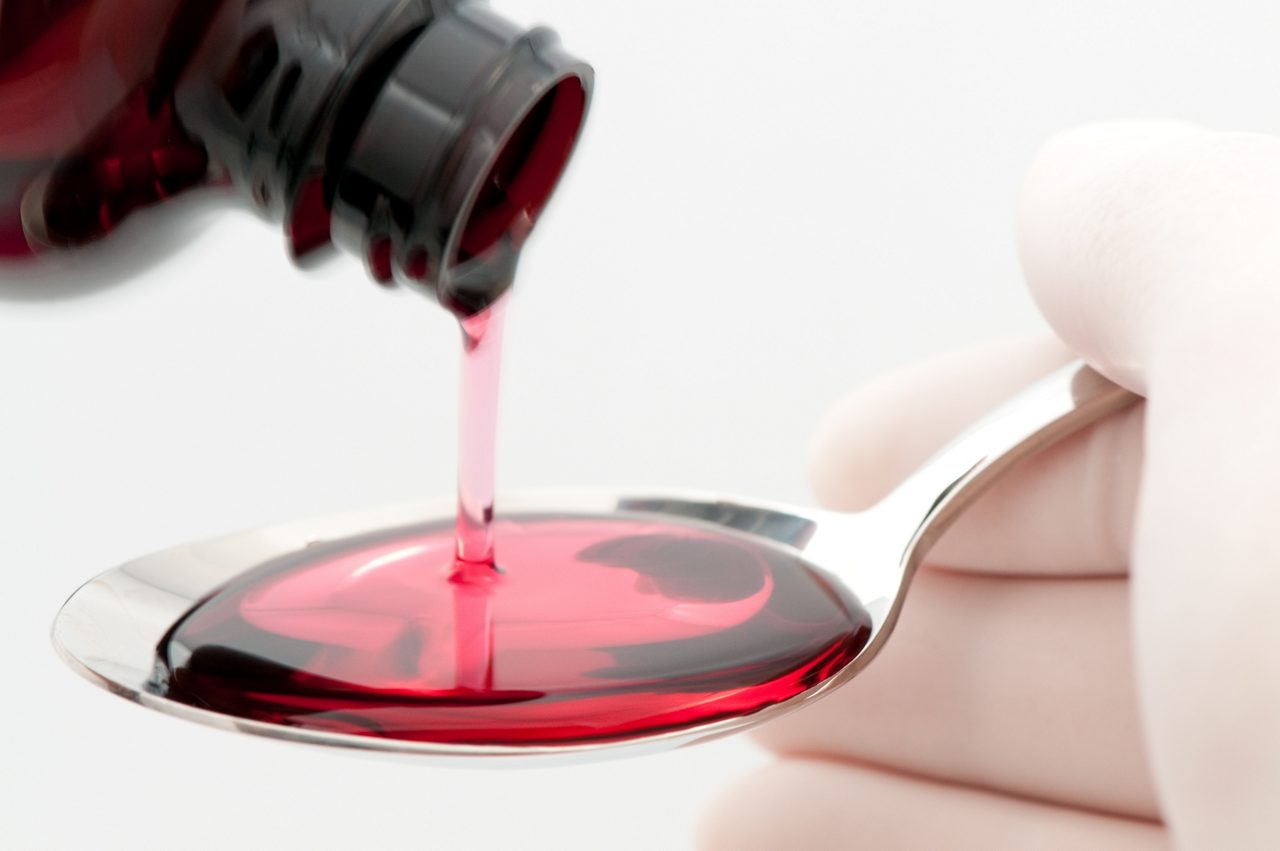 Spoonful of cough syrup being filled by person wearing latex gloves, on white background