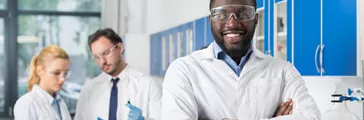 Happy smiling African American scientist standing in front of colleagues in laboratory