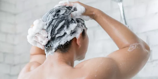 Back view of man washing his air in a large tile shower