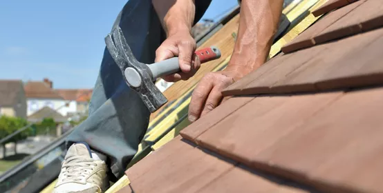 Man working on roof shingles with a hammer.