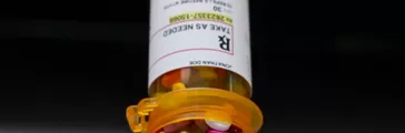 Prescription bottle full of and pouring out wide variety of pills