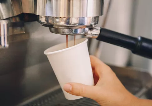 Closeup of young Caucasian barista hands holding paper cup making coffee 