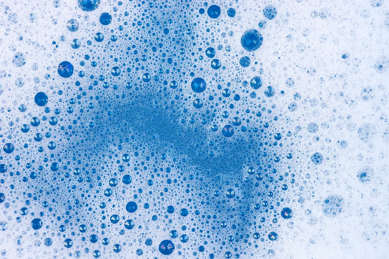 Macro close up photograph of white foam on surface of blue liquid 