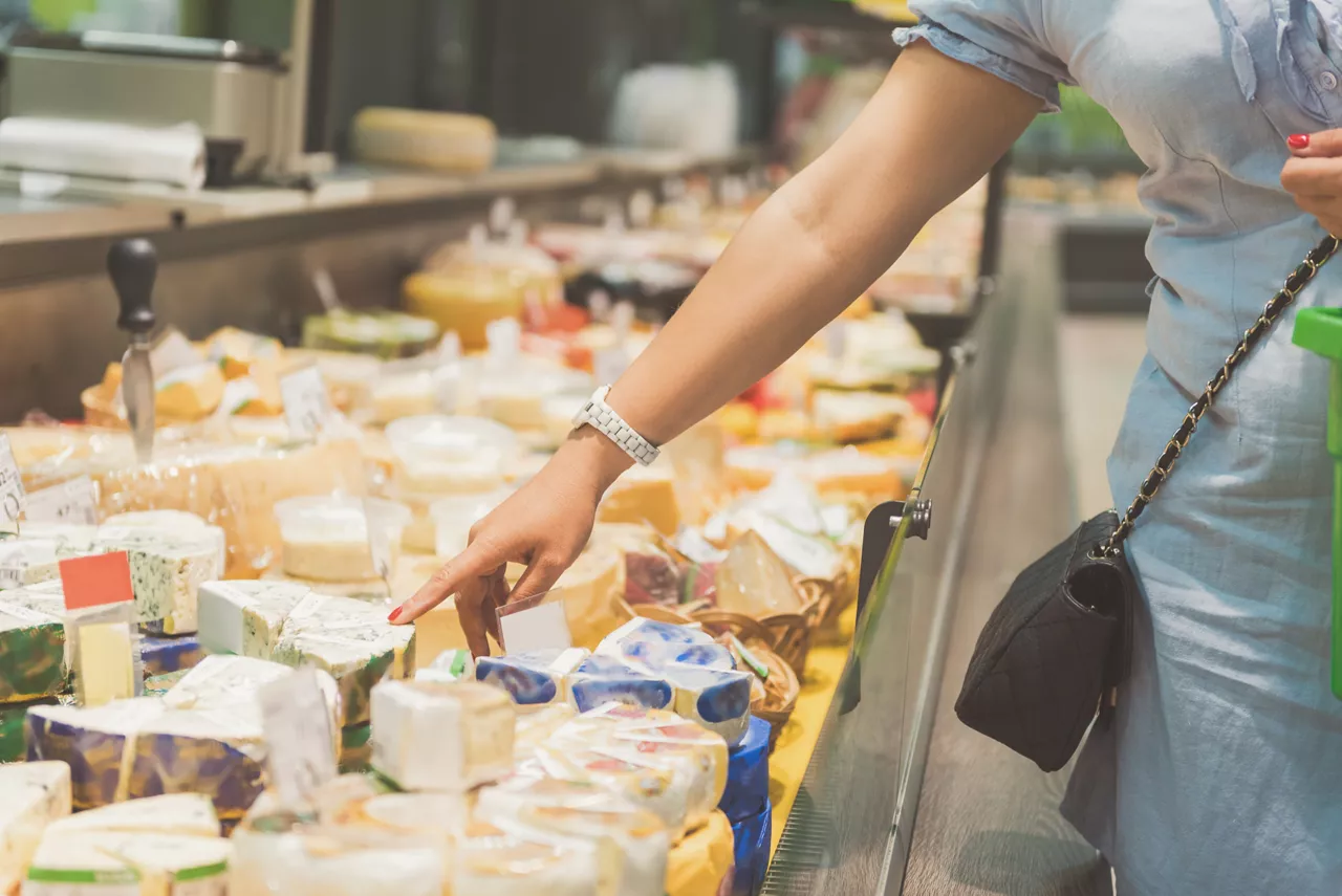 I would like this one. Close up woman hands showing on piece of appetizing cheese in supermarket