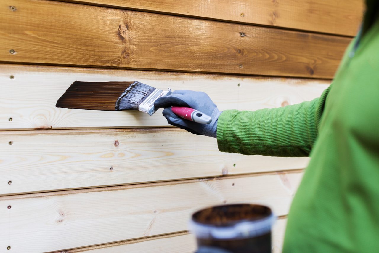 Painter with paintbrush painting house facade with protective color.