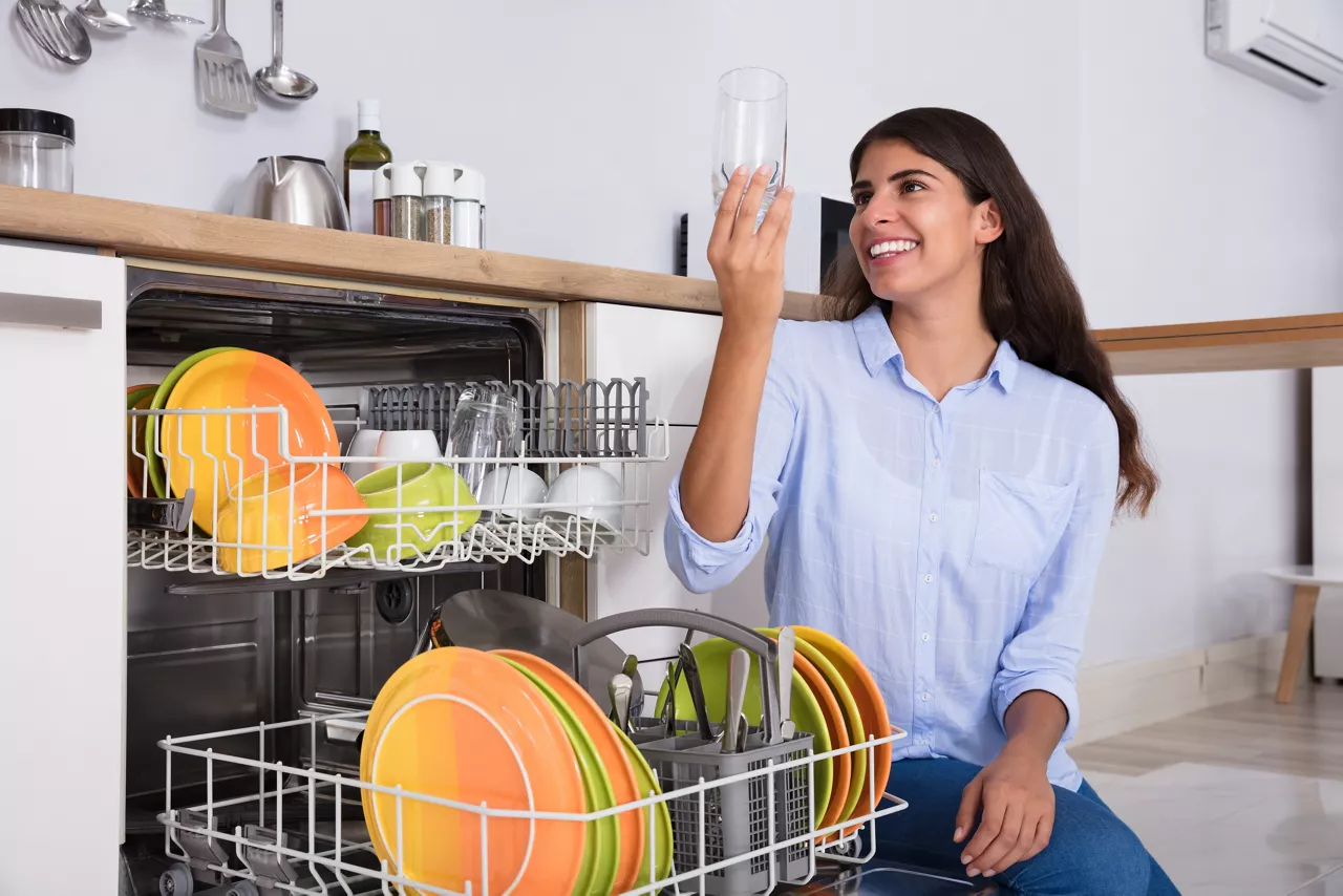 Happy Woman Looking At Clean Glass Crouching Near Dish Washer