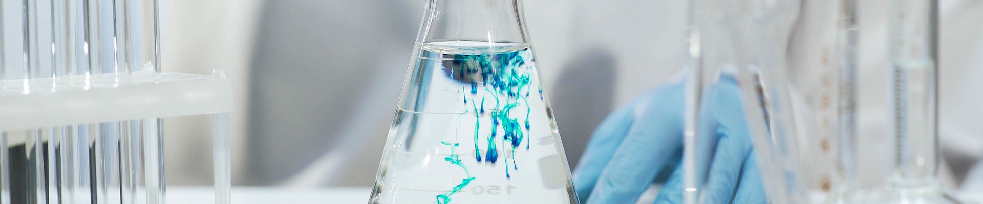 Chemist pouring blue substance into conical flask