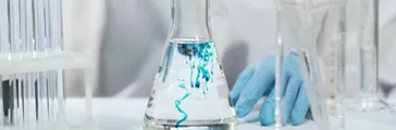 Chemist pouring substance into conical flask with liquid