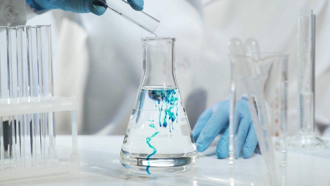 Químico vertiendo la sustancia azul en un matraz cónico