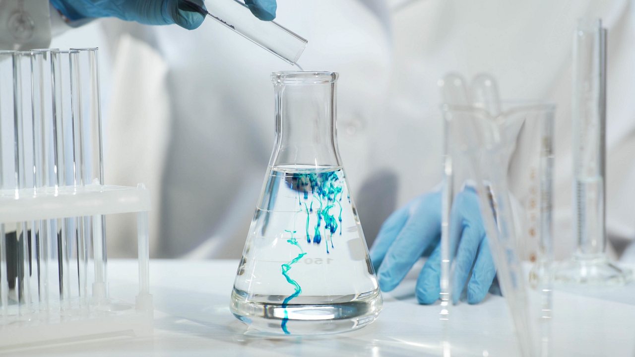 Chemist pouring blue substance into conical flask