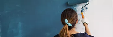 Young woman painting interior wall blue with paint roller