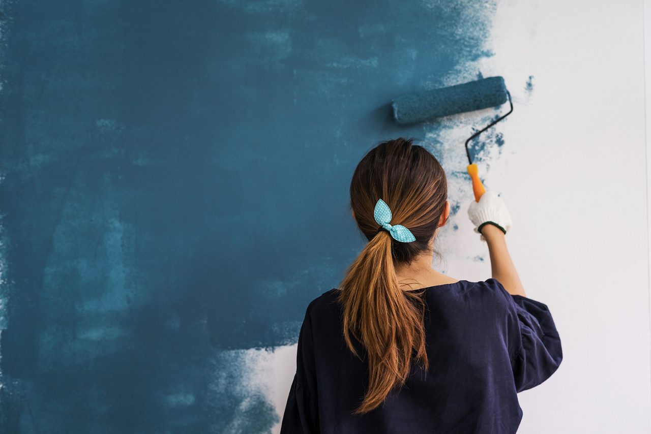 Young woman painting interior wall blue with paint roller