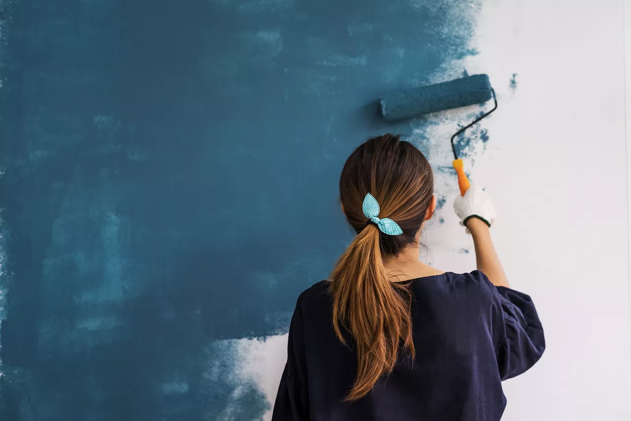 Young woman painting interior wall with paint roller