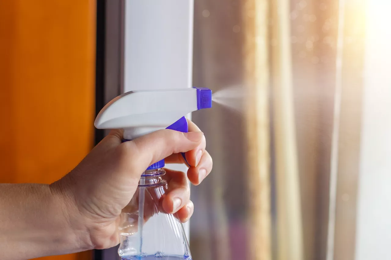 Hand spray sprays cleaner on window in the house