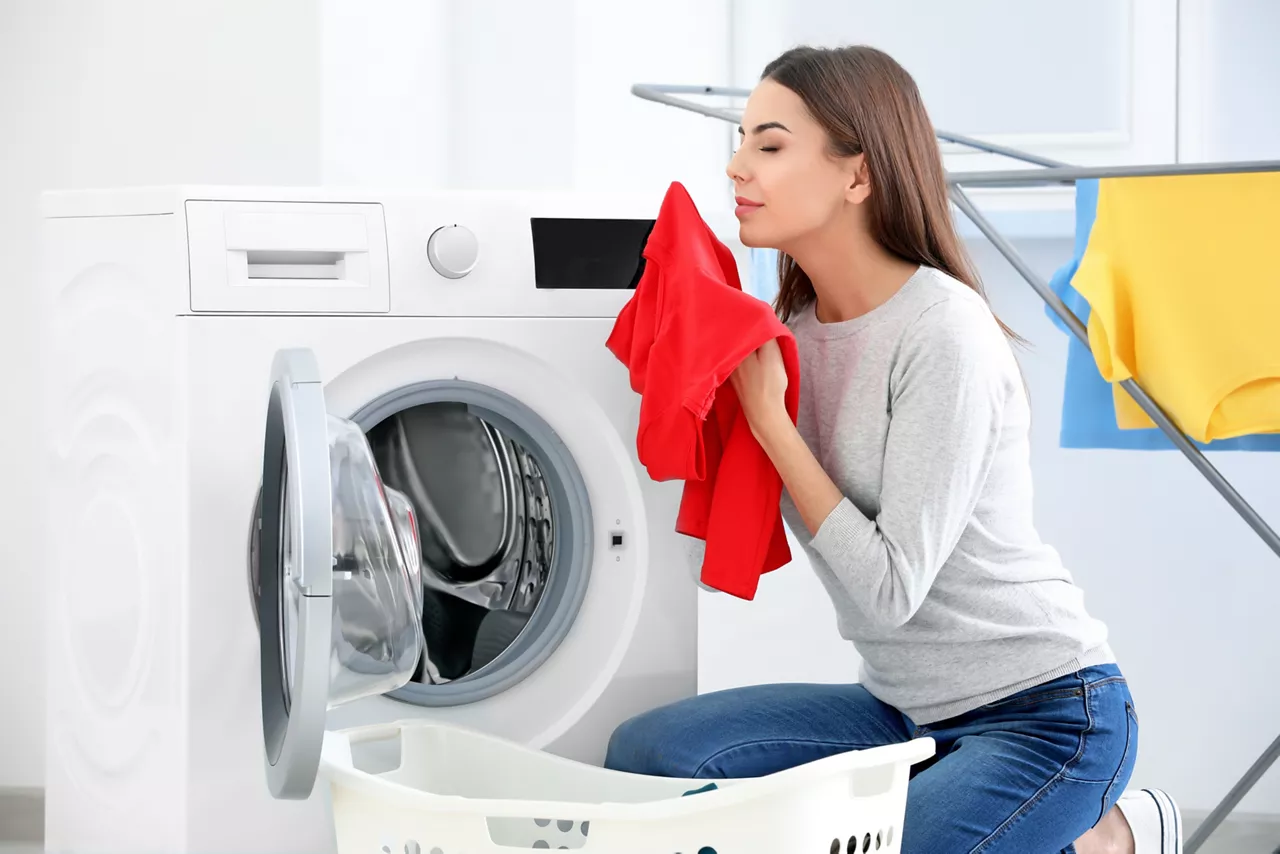 Young woman smelling clean laundry  