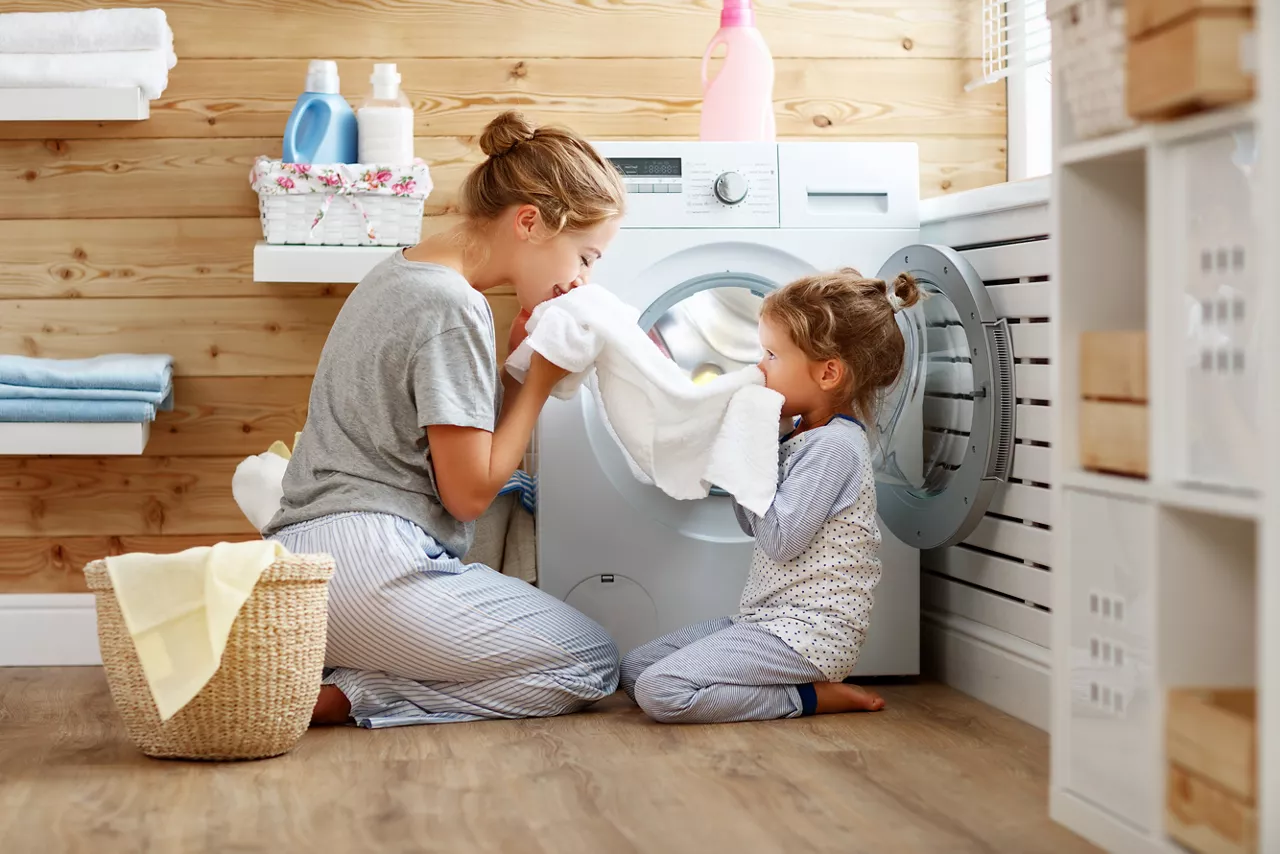 Mother and child daughter in laundry with washing machine 