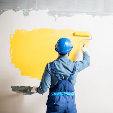 Workman in uniform painting wall with yellow paint at the construction site indoors