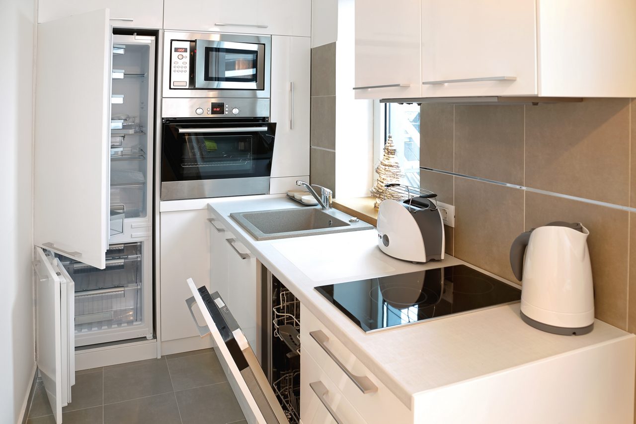 Moderna cocina blanca con todas las puertas de electrodomésticos abiertas 