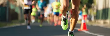 Close up of man's legs and running shoes on asphalt track with blurry marathon runners in background