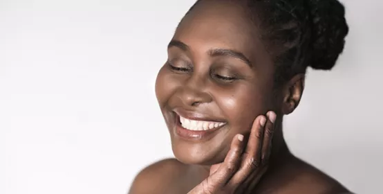 Smiling young plus size African woman standing with her eyes closed against a white background touching her cheek