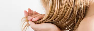 Young woman with hand touching her wet, blonde, perfect hair after shower on the white background. Care about beautiful, healthy and clean hair. Beauty salon concept. Side view.