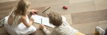 Kids drawing together on wooden warm floor in living room