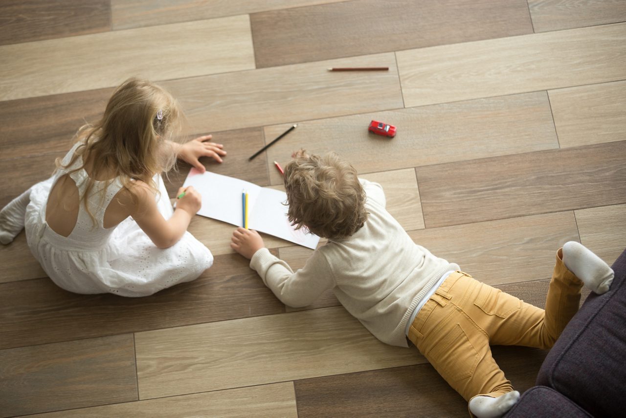 Niños jugando a dibujar juntos en el piso de su casa, vista superior 