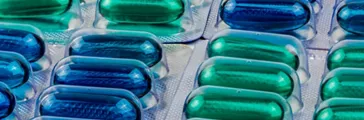 Macro shot detail of blue and green soft gel capsule pills in blister pack.
