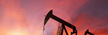 Pump jack silhouette against a sunset sky with deliberate lens flare and copy space